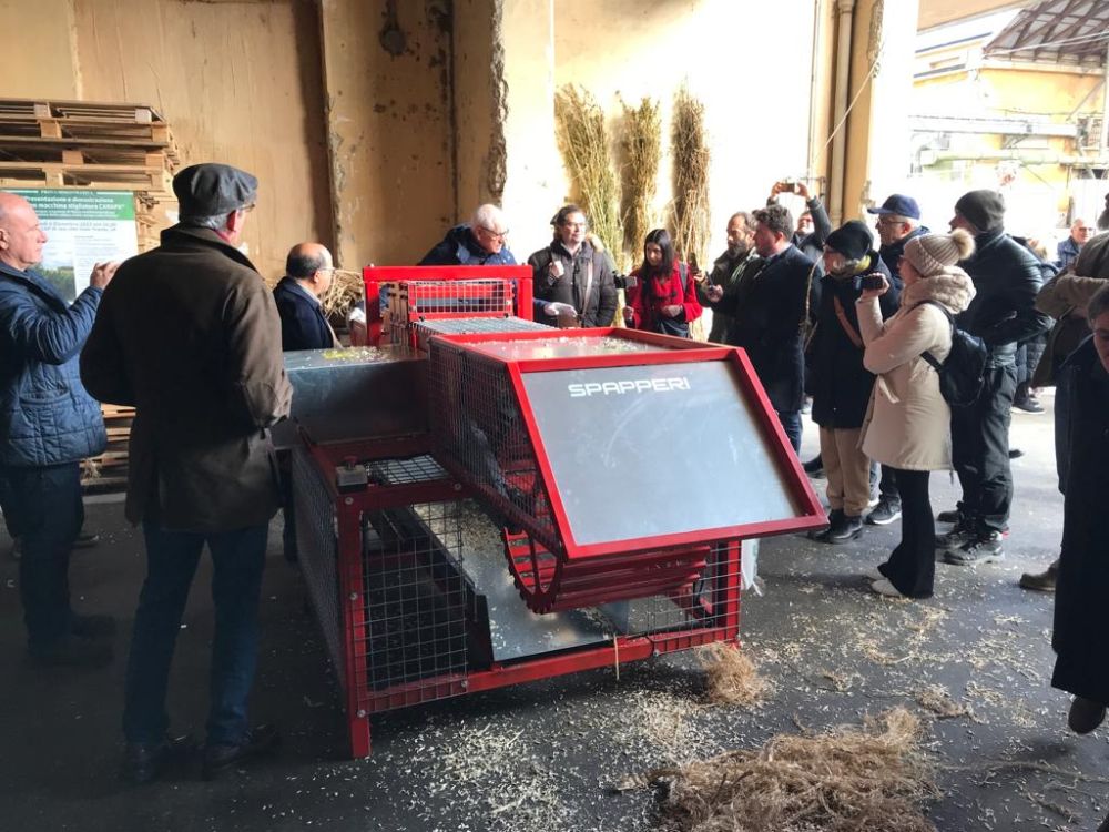 Nell'immagine sono presenti i visitatori al consorzio agrario di Jesi che stanno osservando una nuova macchina per la lavorazione della canapa